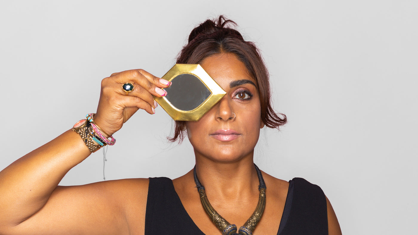 Founder Amina holding up small eye shaped Moroccan mirror in front of one eye