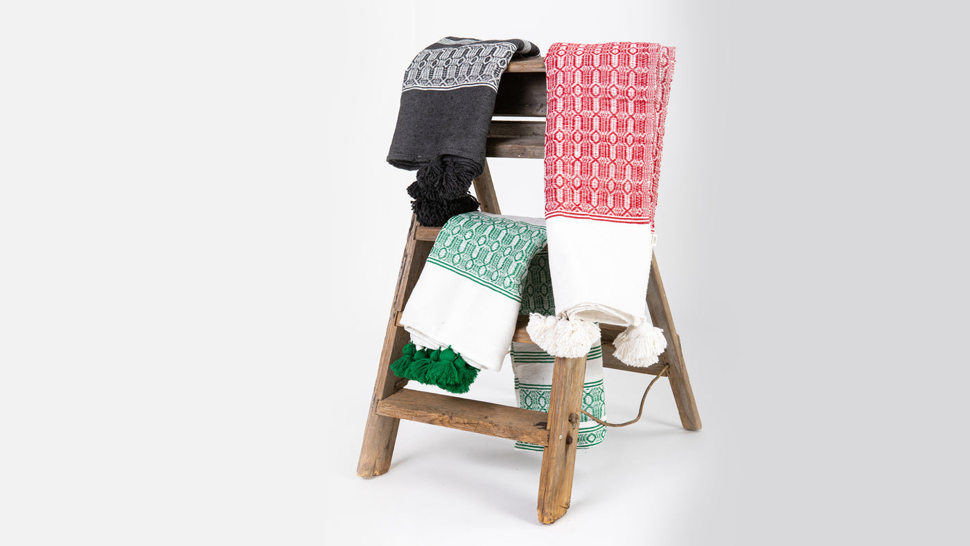 3 cotton rugs, red, black and green, folded and draped over a rustic wooden step ladder